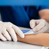Person wearing gloves applying a bandage to a child's arm on a blue background