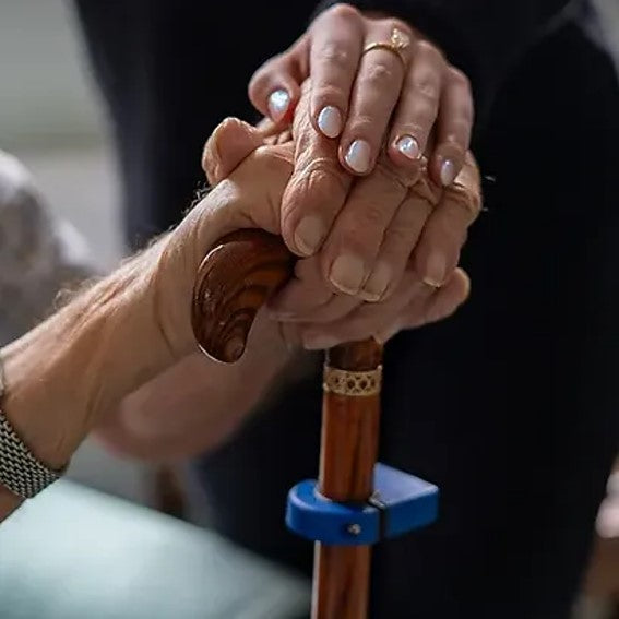 A woman clasps the hand of an elderly person, representing the bond of care and assistance in their shared journey